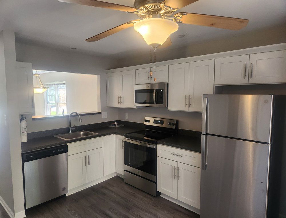 Modern kitchen with white cabinets, stainless steel appliances, ceiling fan, and laminate wood flooring.