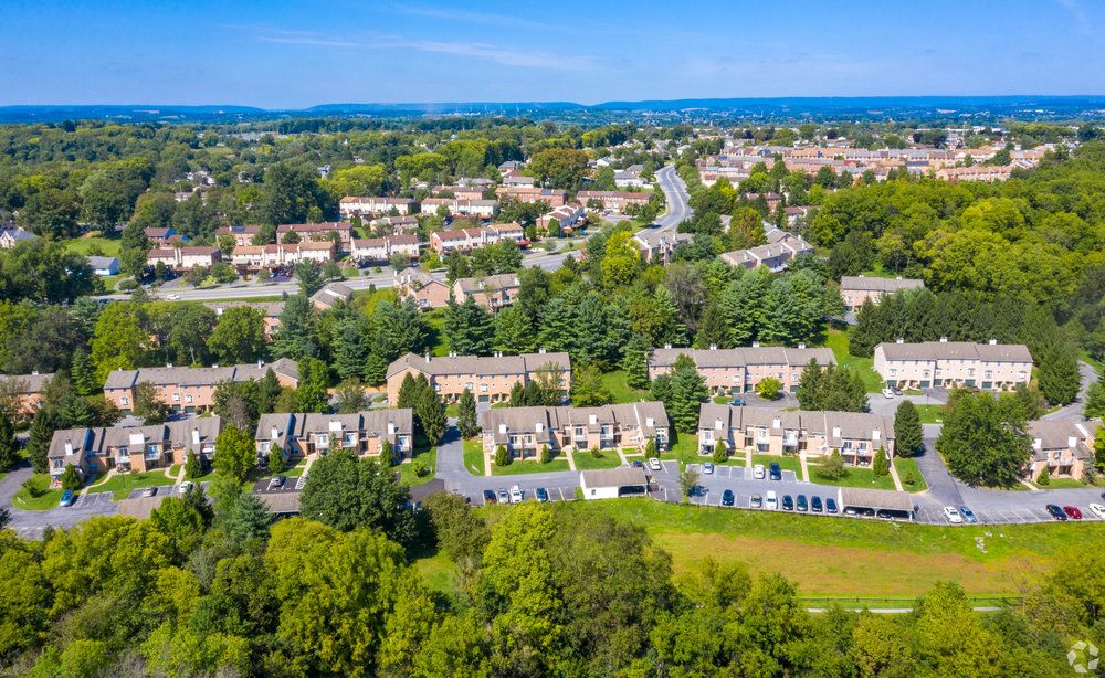 Aerial view of a suburban neighborhood with rows of houses, trees, and roads on a clear day.