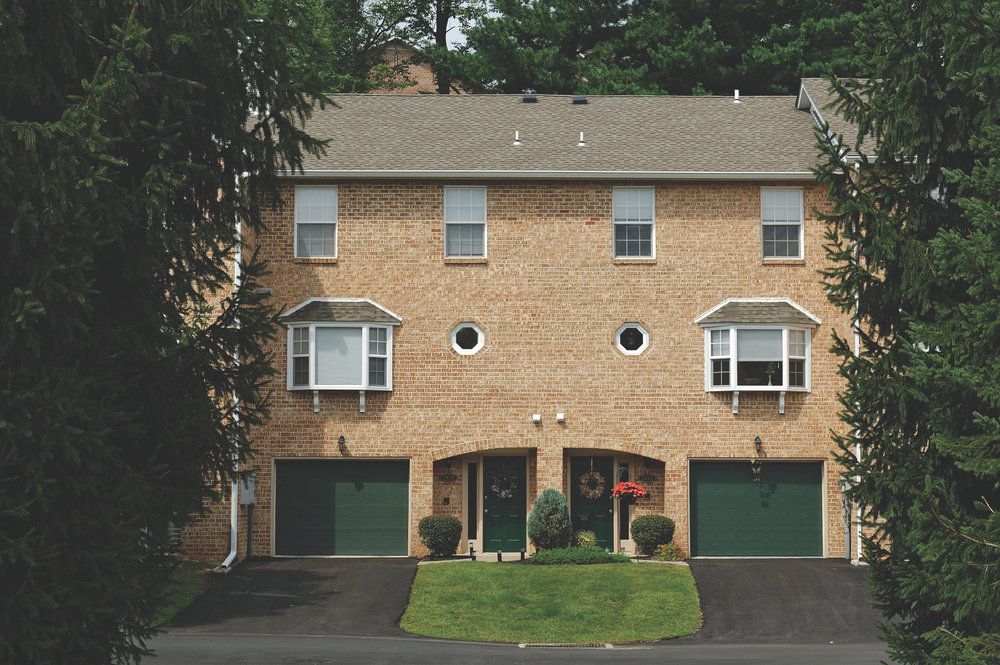 Three-story brick townhouse with two green garage doors, bay windows, and circular windows above.