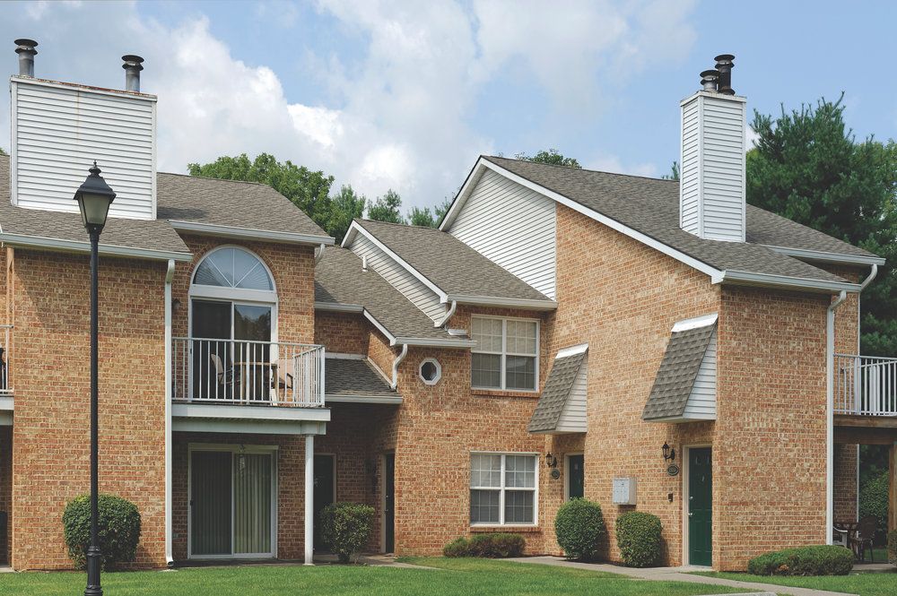 Two-story brick apartment building with balconies, white trim, and manicured lawn on a sunny day.