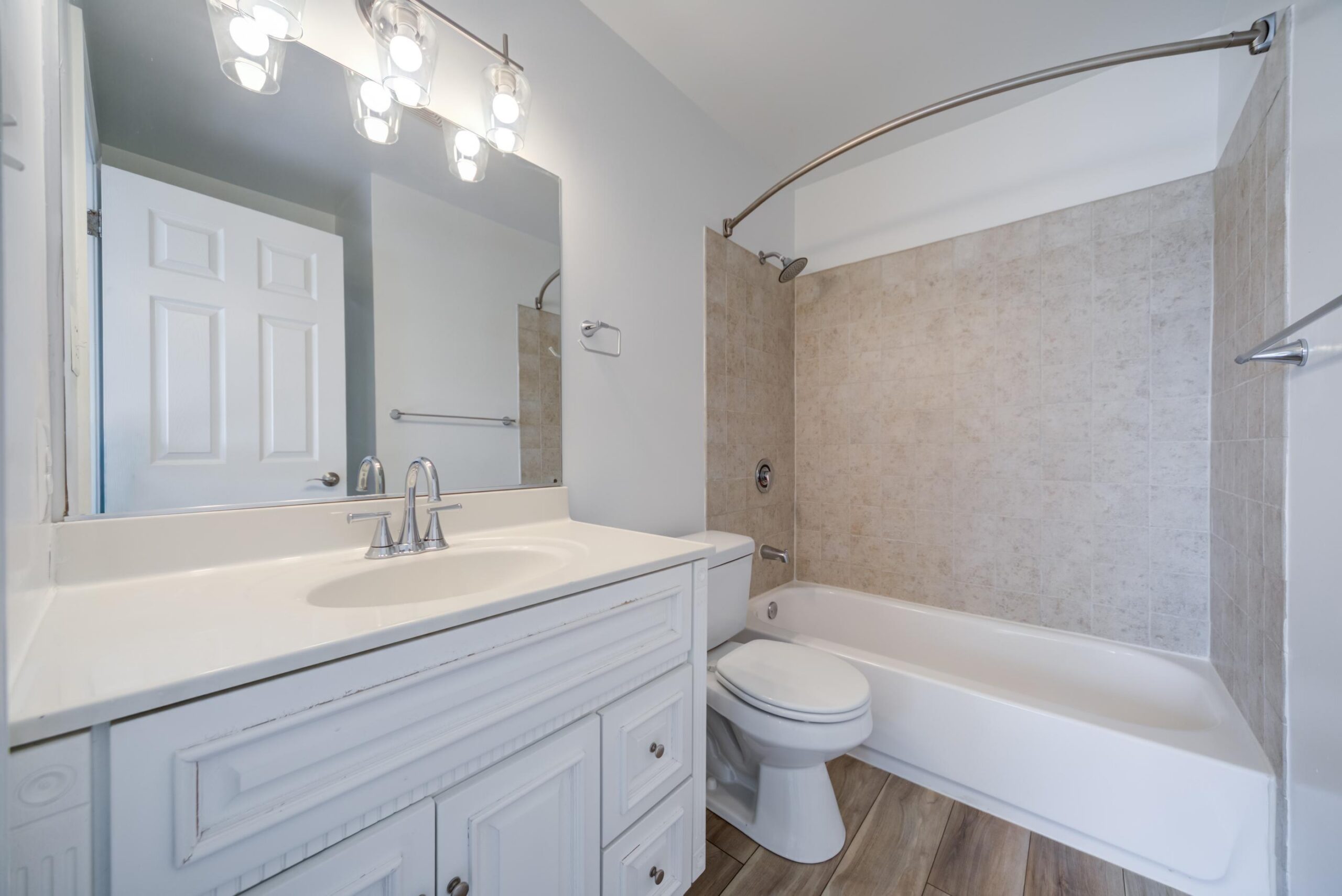 Bathroom with a white vanity, a toilet, and a bathtub with a tiled surround.